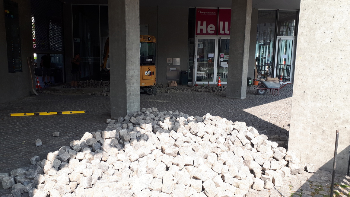 ein ungeordneter Haufen loser Pflastersteine in der Sonne, umrahmt von einigen Betonsäulen