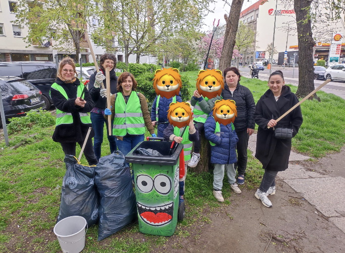 Menschengruppe mit Müllzangen und Mülltonne auf einer Grünfläche